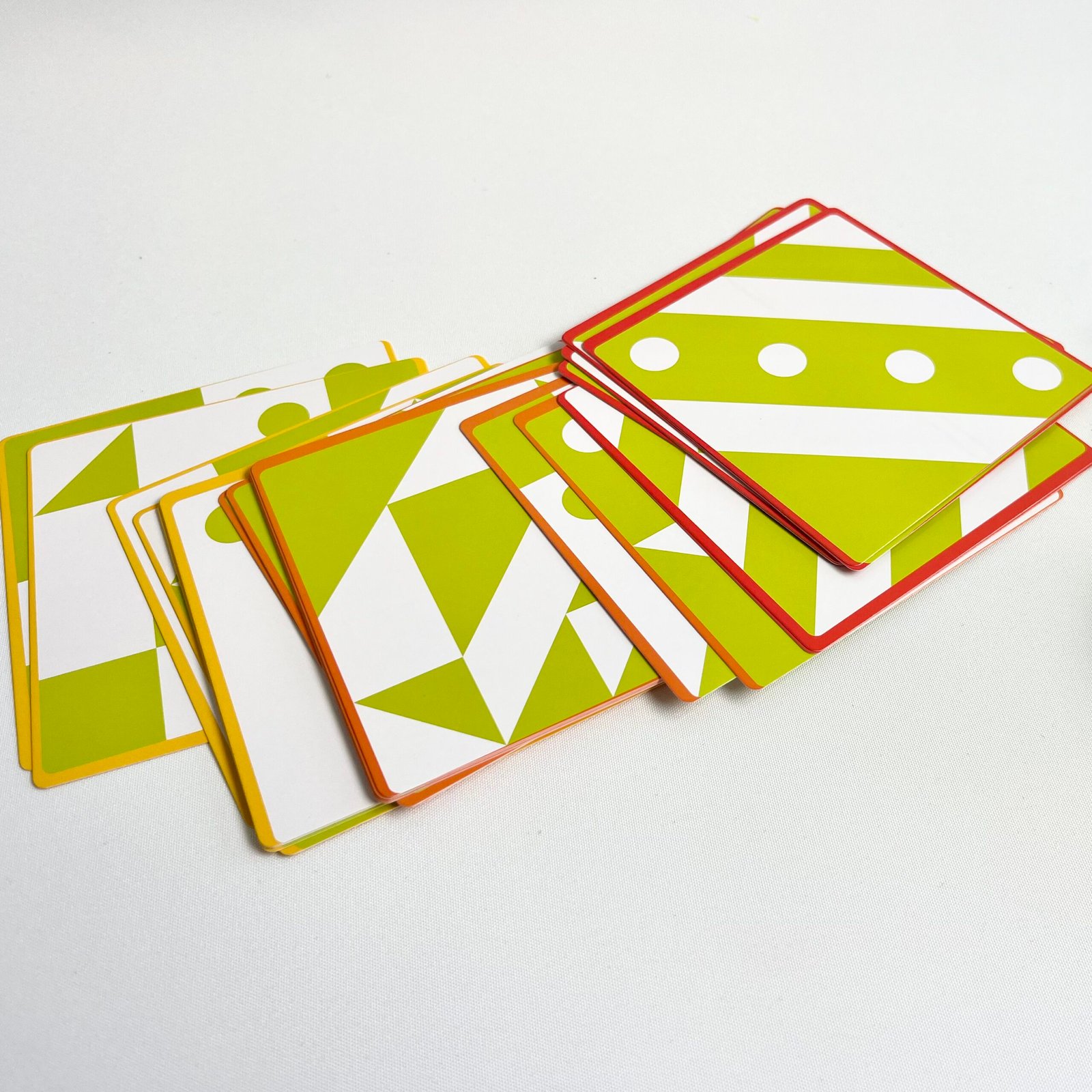 3D-jigsaw-puzzle-cards A fanned arrangement of the colourful challenge cards for the 3D Wooden Visual Perception Puzzle, showcasing various green, white, and yellow patterns with orange and red borders, on a white surface.