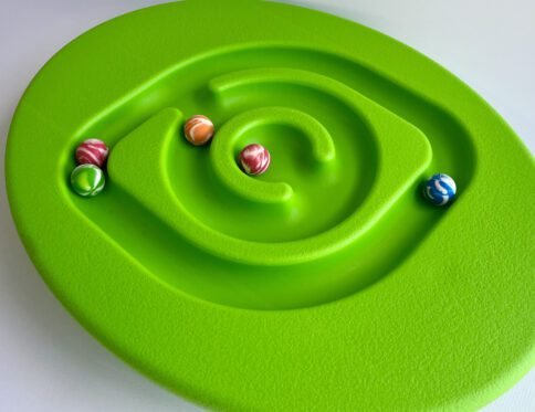 Top-down view of a bright green oval balance board with a spiral ball maze, featuring five colourful marbles placed within the maze tracks.