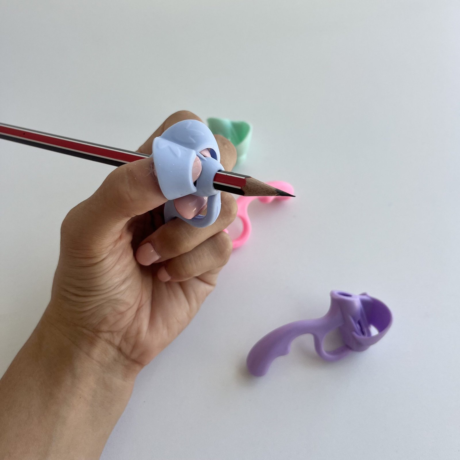 Close-up of a hand comfortably holding a pencil with the light blue 5-finger pencil grip corrector, illustrating correct finger placement for an effective pencil grip.