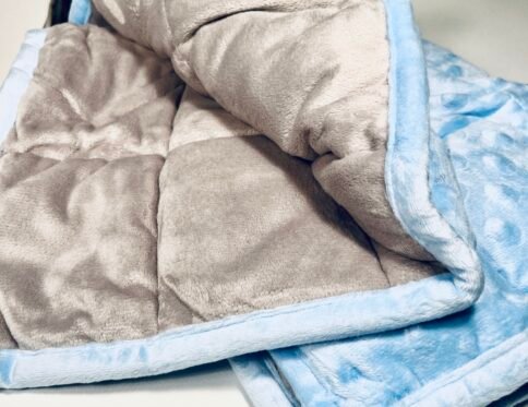 Close-up view of a folded soft weighted lap pad, showing the plush blue minky fabric with dimples and the smooth grey reverse side.