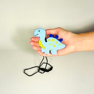 Child's hand holding a light blue and yellow dinosaur sensory chew necklace with a black safety cord.