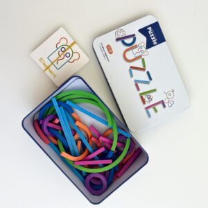 Overhead view of the open 'Skilful Puzzle' tin filled with various colourful wooden stick puzzle pieces (straight, curved, rings), with a white challenge card showing an elephant beside it.