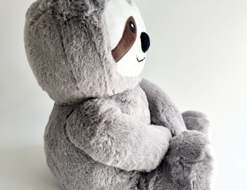 Side profile of the plush grey weighted sloth teddy, showing its soft texture and relaxed sitting pose against a white background.