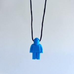 Close-up, front view of a vibrant blue Lego man chewable pendant on a black adjustable cord, showing the texture of the cord and the smiling face detail.