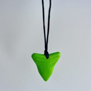 A single green chewable necklace shaped like a shark tooth, hanging on a black cord against a light grey background.