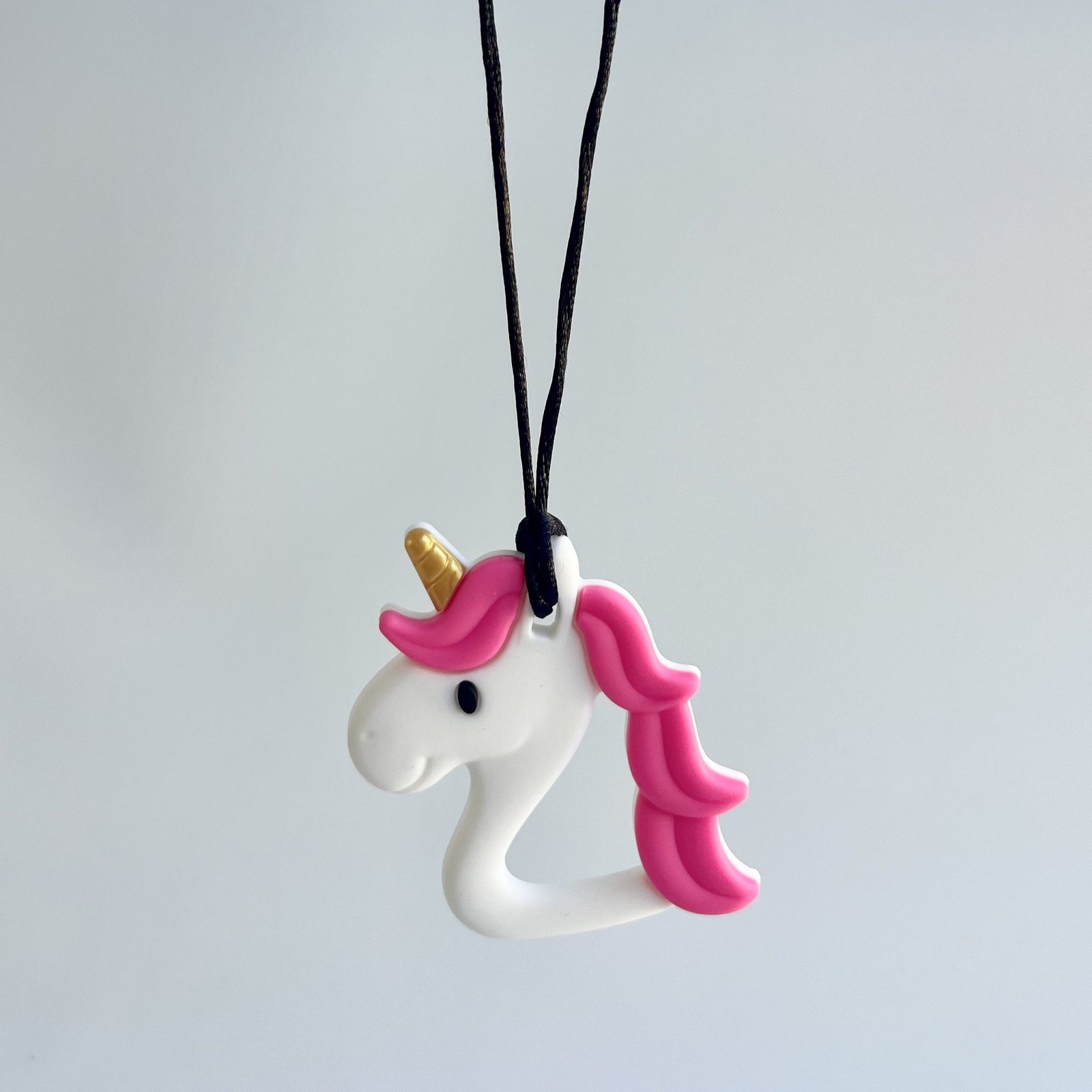 A single white unicorn-shaped chewable necklace with pink mane/tail and gold horn, hanging on a black cord against a light grey background.
