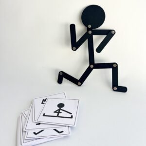 wooden-man-running Overhead view of the black Pose & Play Wooden Man articulated figure in a running pose, with a stack of black and white body pose challenge cards lying below it on a white background.