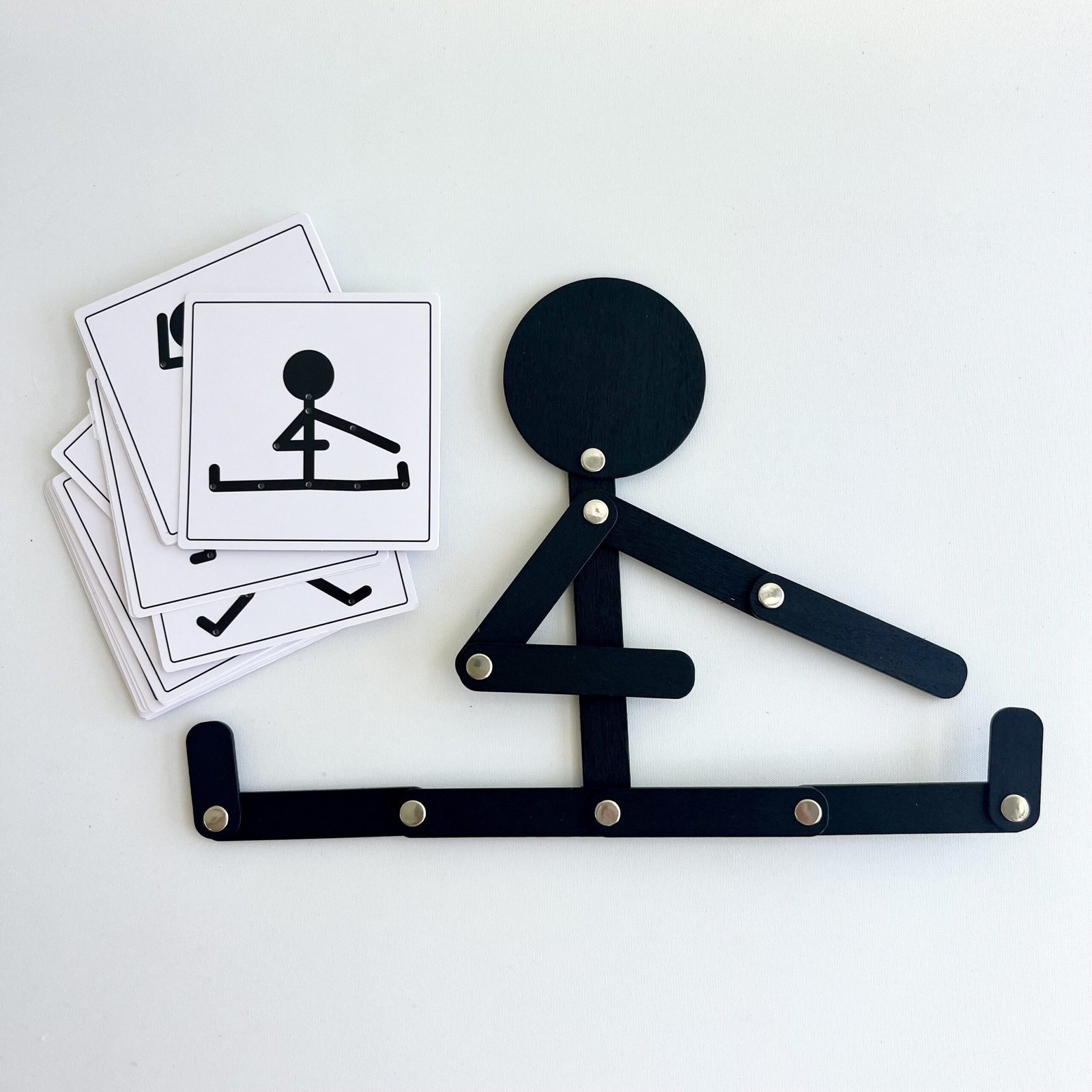 wooden-man-stretching Overhead view of the black Pose & Play Wooden Man articulated figure sitting in a split pose, next to a stack of black and white body pose challenge cards on a white background.