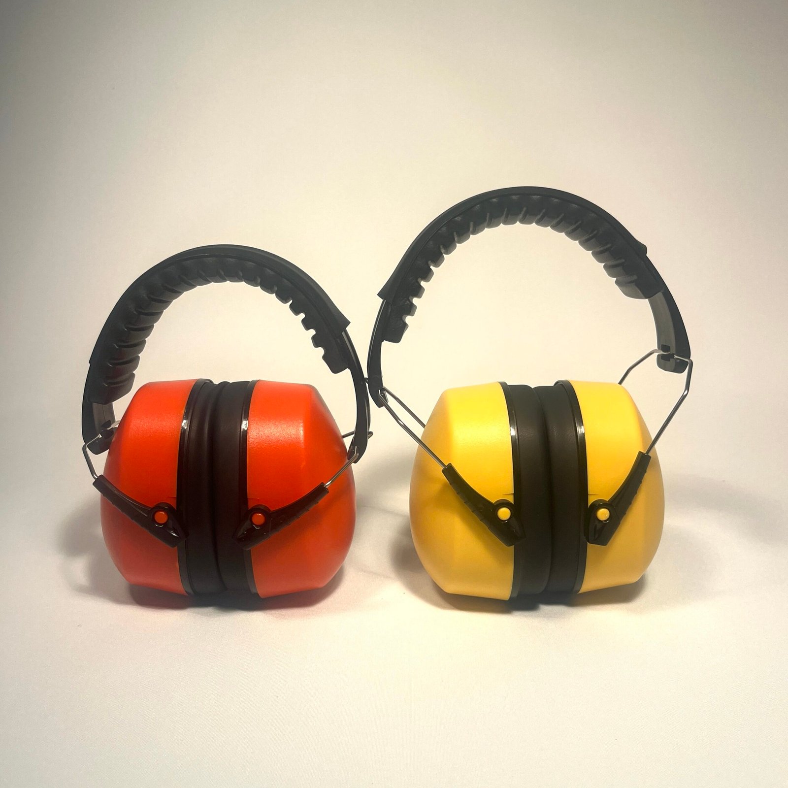 Side-by-side view of two pairs of noise cancelling headphones for children, one bright orange and one bright yellow, both with black headbands and earcups.