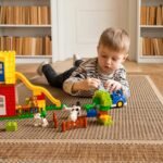 Young boy engaged in imaginative block play on a carpeted floor indoors.