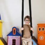 Boy in glasses swinging indoors with colorful cardboard castles.