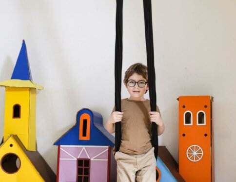Boy in glasses swinging indoors with colorful cardboard castles.