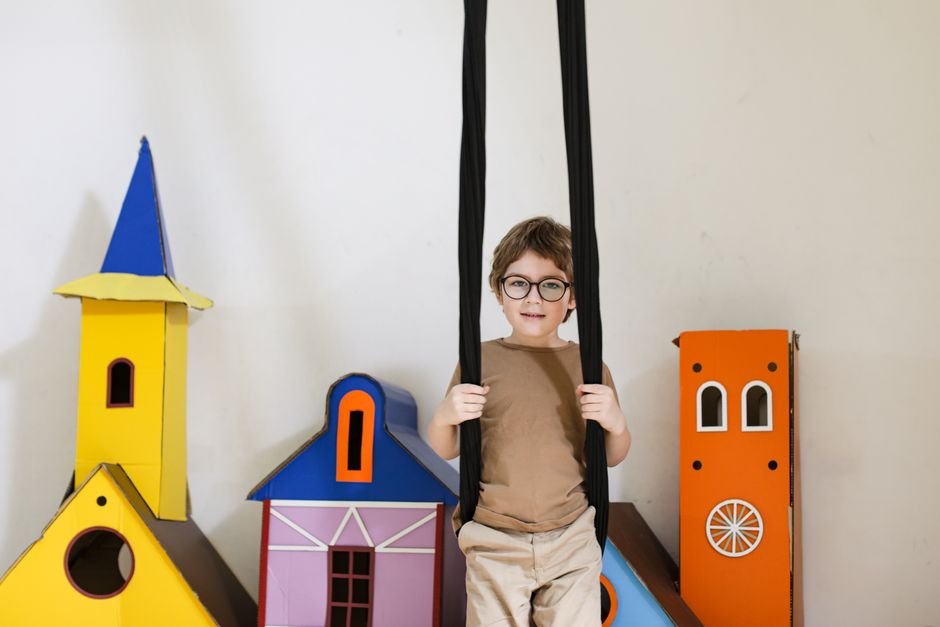 Boy in glasses swinging indoors with colorful cardboard castles.